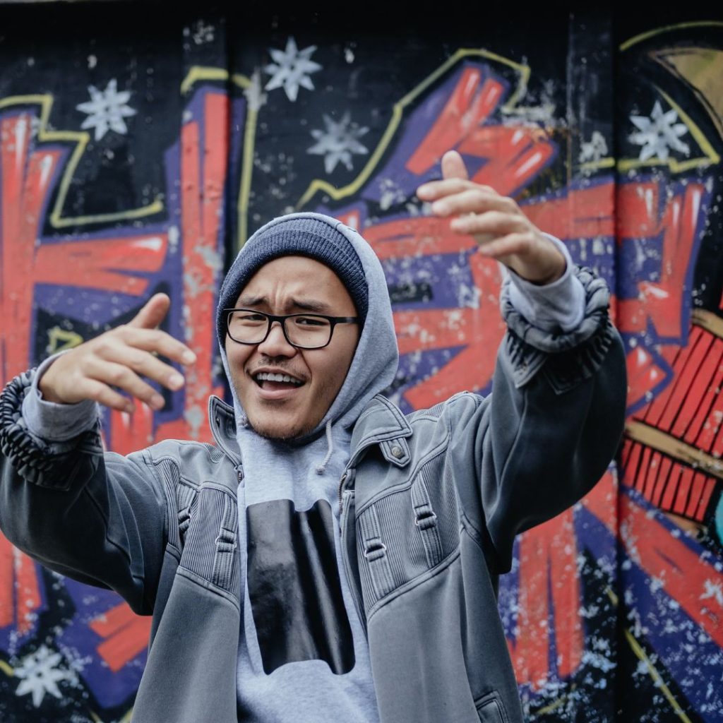 boombap style rapper standing in front of a graffiti